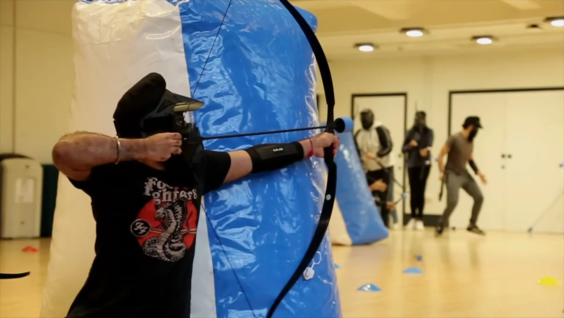 A masked player draws a bow beside a blue inflatable bunker
